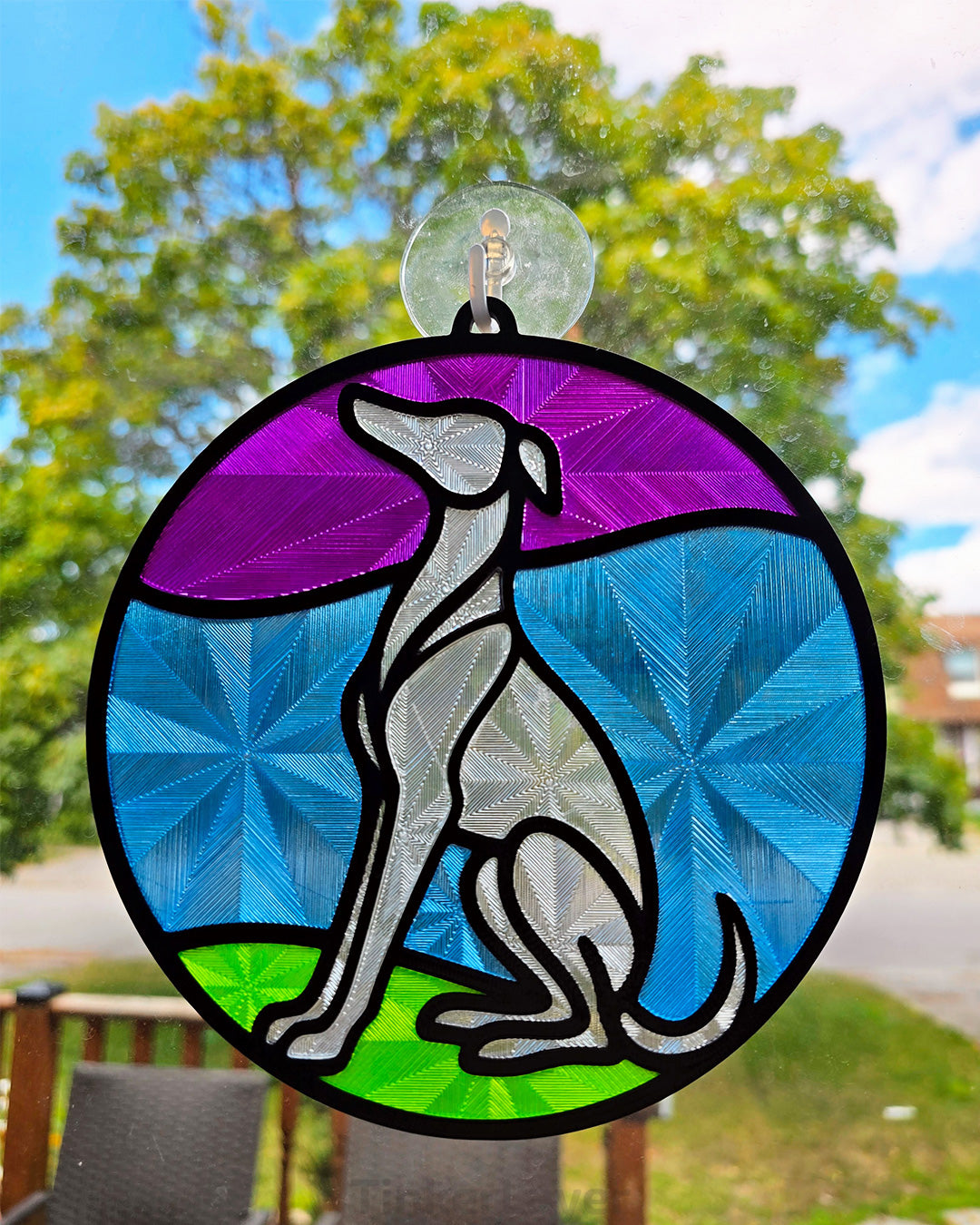 Round whippet stained glass style suncatcher with purple, blue, and green accents hanging in a window